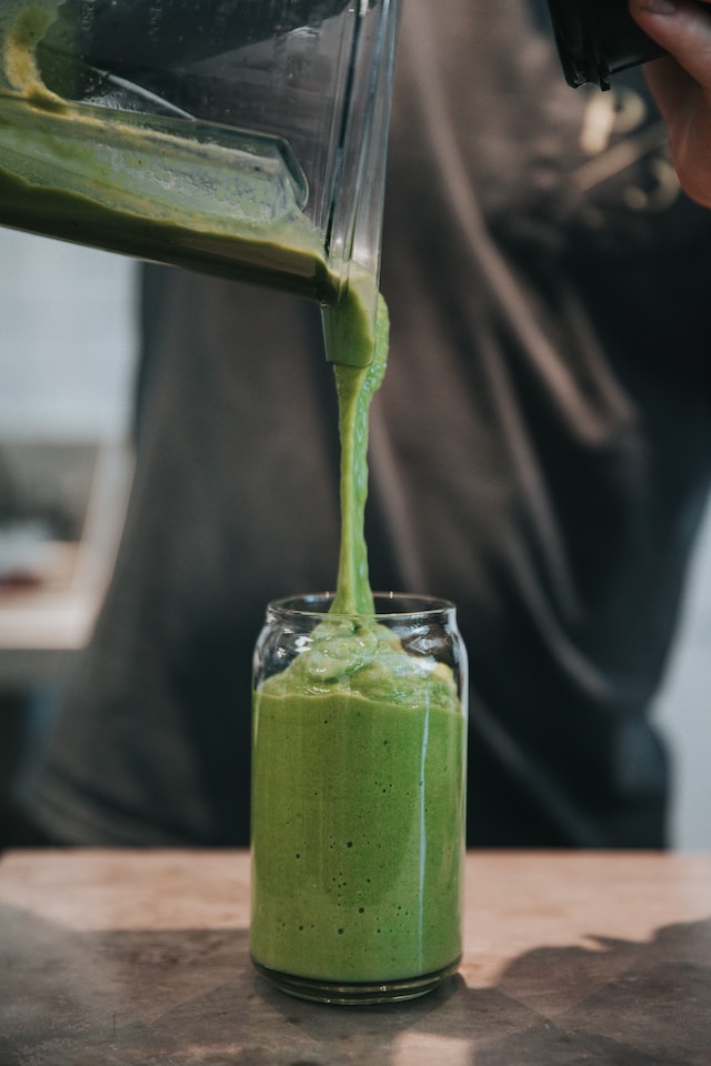 Person pouring green smoothie in glass